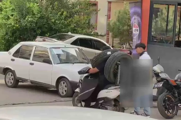 Otomobil lastiğini boynuna asan kuryenin ilginç taşıma yöntemi kameraya yansıdı
