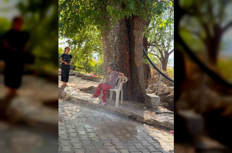 Kavurucu sıcağa karşı çözümü ağaçtan sarkıttığı hortumdan akan suda buldu